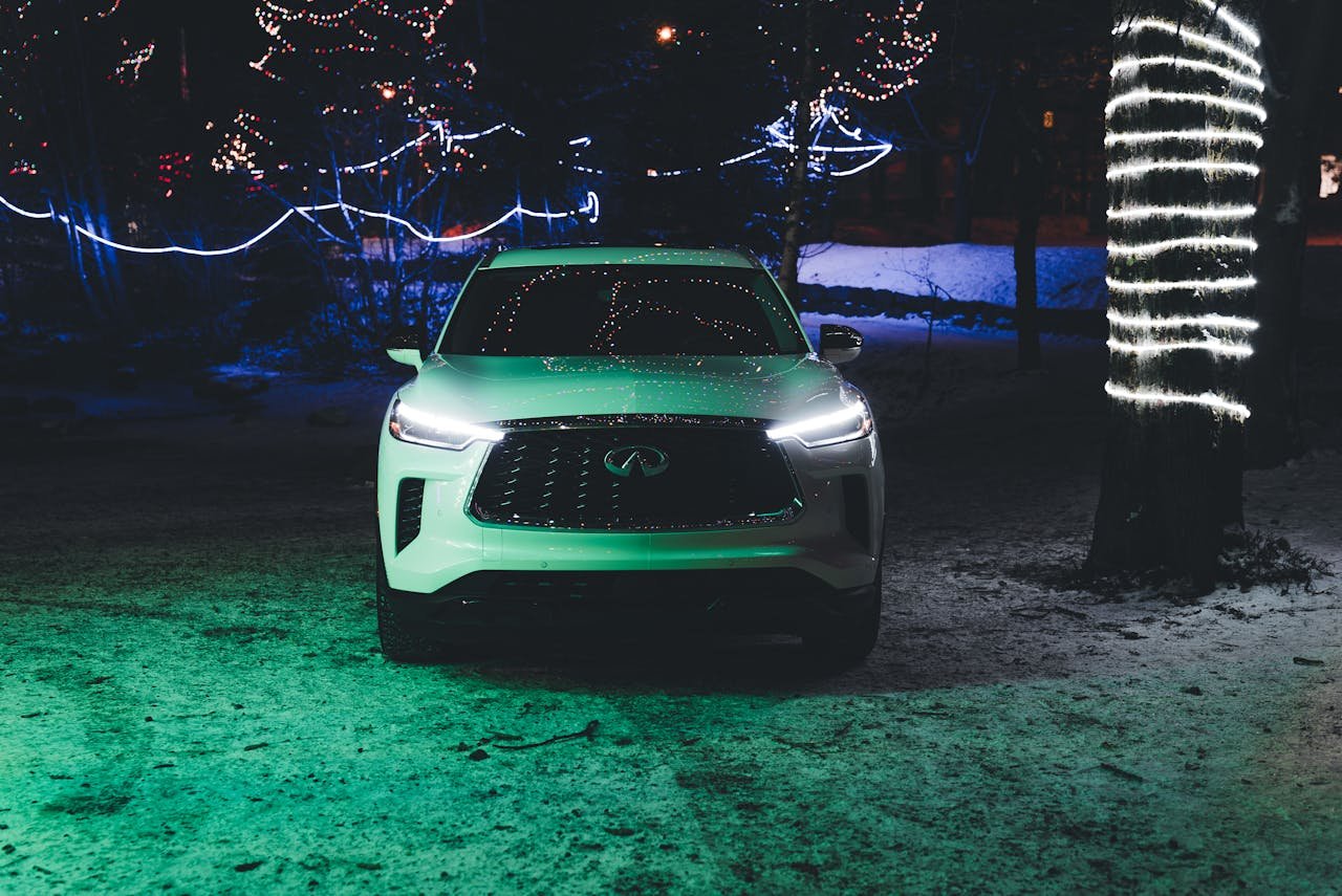 A white SUV parked outdoors at night with festive Christmas lights illuminating the snowy scene.