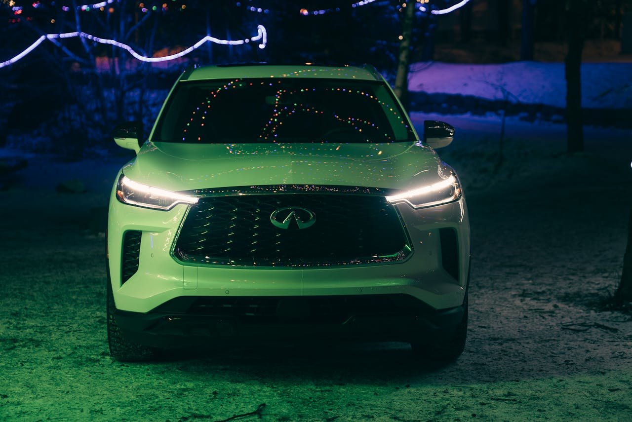 Front view of a luxurious Infiniti SUV with headlights shining, surrounded by night lights.