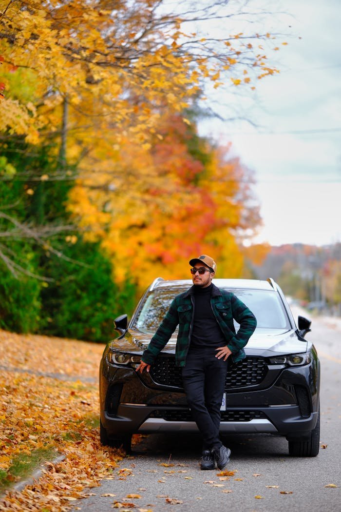 Man leans on car amid colorful autumn foliage in Huntsville, Ontario, Canada.
