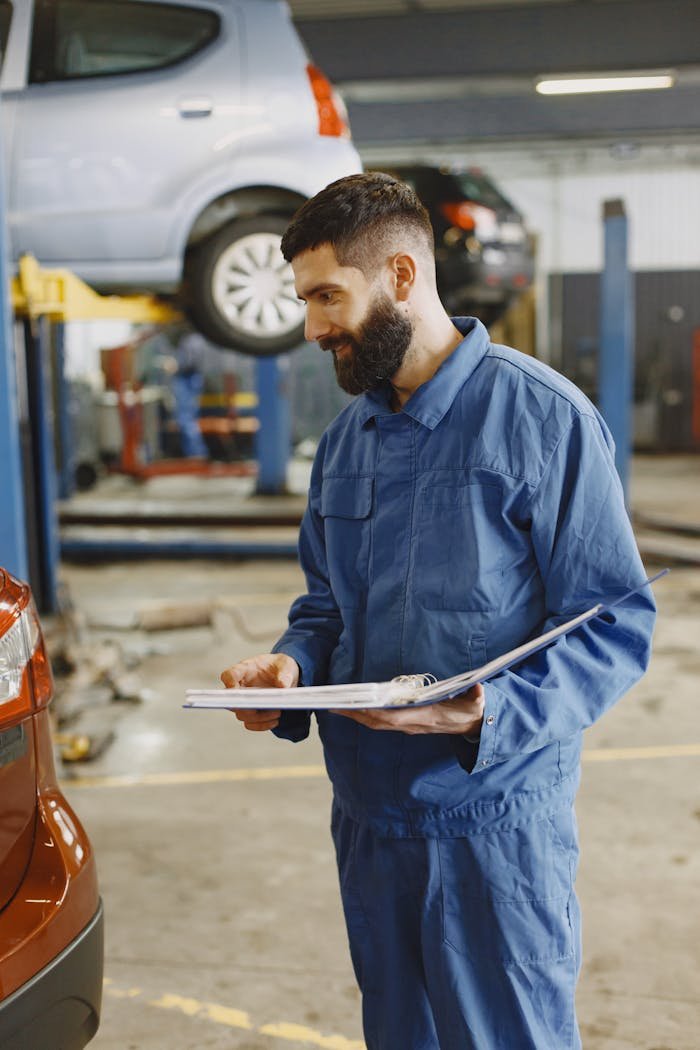 Mechanic in blue coverall examining documents in a bustling auto workshop.